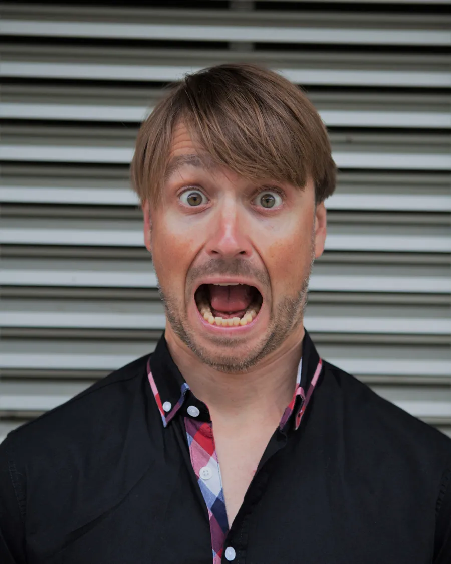 Andy Sauerwein mit weit aufgerissenem Mund und großen Augen vor einer Metalljalousie